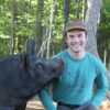 Evan Streeter is pictured here on his farm with one of his hogs. Woods are in the background. Streeter raises pigs the way nature intended, with animal happiness and conservation as a top priority.