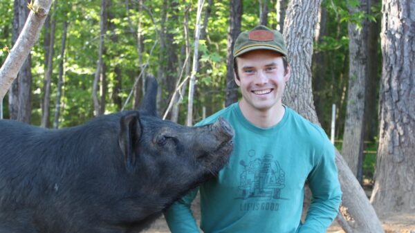 Evan Streeter is pictured here on his farm with one of his hogs. Woods are in the background. Streeter raises pigs the way nature intended, with animal happiness and conservation as a top priority.