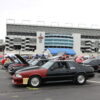 Ford Mustangs line in rows in front of Coca Cola sign at Charlotte Motor Speedway